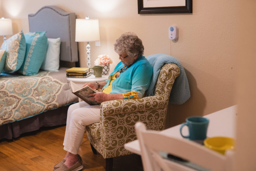 the_colonnade_at_carrollwood-127 - Anthem Lakes Senior Living Senior woman sitting in bedroom chair reading