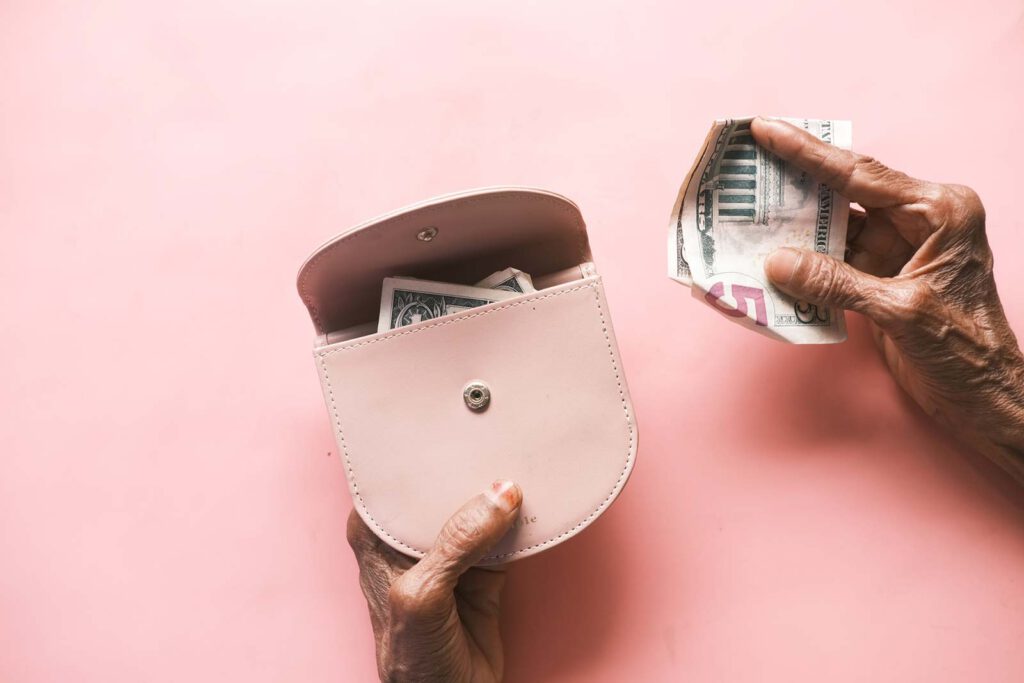 blog-current-scams-targeting-seniors-and-how-to-avoid-them.jpg - Anthem Lakes Senior Living Close up of a senior holding a pink coin purse with money visible inside