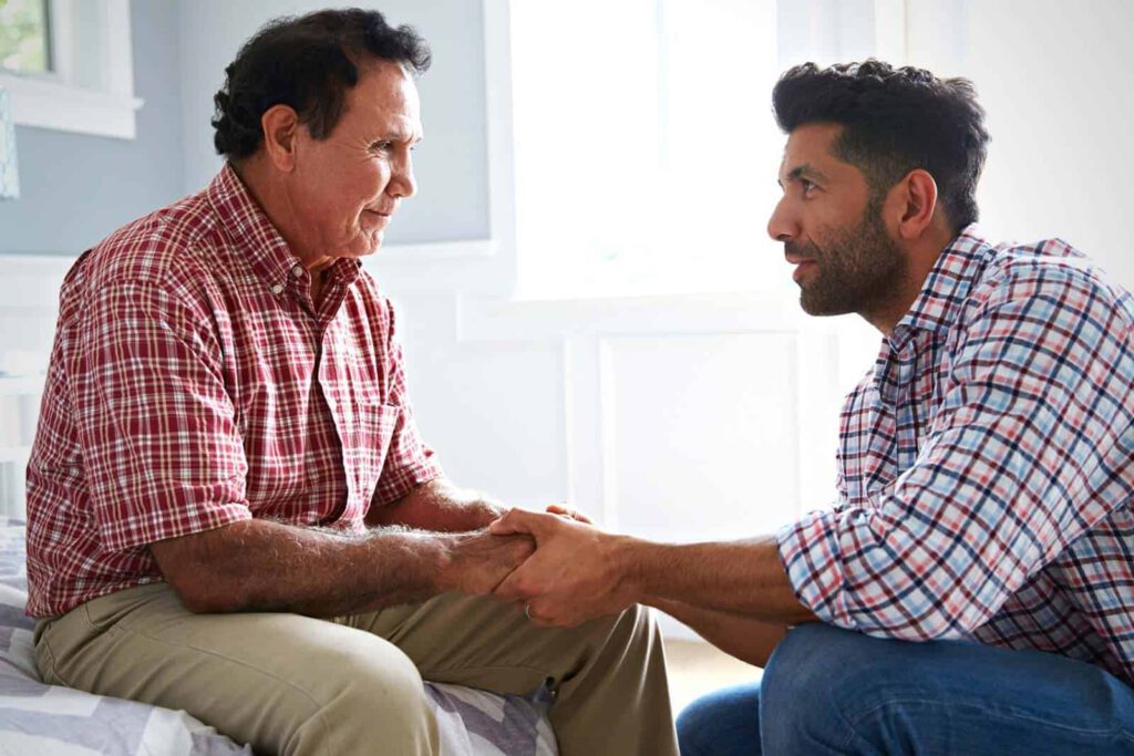 blog-world-alzheimers-month-2021.jpg - Anthem Lakes Senior Living Senior man seated with adult man kneeling beside him holding his hand